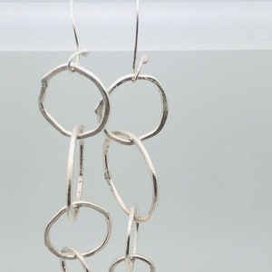 May include: Silver dangle earrings with multiple interconnected circles. The circles are of varying sizes and have a hammered texture.