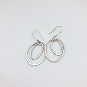 May include: A pair of silver earrings with a double oval design. The ovals are slightly textured and have a hammered finish.