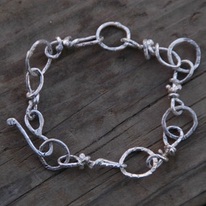 May include: A silver bracelet with a unique, twisted design. The bracelet is made of interconnected loops and circles, creating a textured and intricate look.