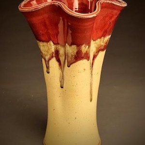 May include: A ceramic vase with a ruffled top and a drip glaze design. The vase is a light yellow color with a red and brown glaze on the top.