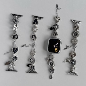 Peut inclure: Bracelets de montre argentés avec des breloques décoratives. Les bracelets présentent divers ornements, notamment des cœurs, des fleurs et des formes géométriques. L'un des bracelets est fixé à une Apple Watch argentée avec un écran noir affichant l'heure.