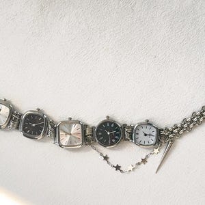 May include: A silver chain bracelet with five square-shaped watches attached. The watches have silver bands and white, black, and silver faces. The bracelet has a star charm and a small silver charm.