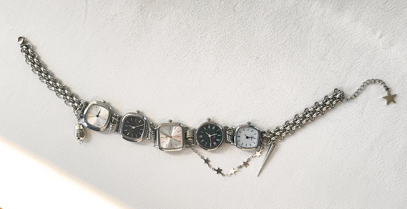 May include: A silver chain bracelet with five square-shaped watches attached. The watches have silver bands and white, black, and silver faces. The bracelet has a star charm and a small silver charm.