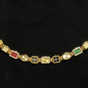 May include: A gold-toned watch bracelet with multiple rectangular and oval watch faces. The watch faces feature various colors, including red, green, and black, and are adorned with small crystals. The bracelet has two circular clasps.