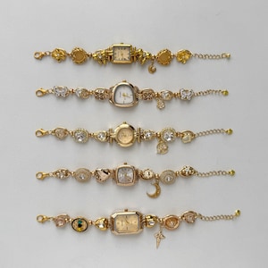 Może przedstawiać: Pięć złotych zegarków na rękę o różnych kształtach tarczy i ozdobnych paskach. Paski zdobione są zawieszkami, kryształami i ozdobnymi ogniwami. Każdy zegarek ma inny wzór tarczy, w tym kształty kwadratowe, owalne i okrągłe.