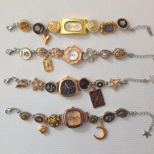 May include: Three gold-tone charm bracelets with watches. Each bracelet features a variety of charms, including flowers, stars, and geometric shapes. The watches have different coloured faces and are all in a square shape.