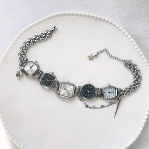 May include: A silver chain bracelet with four square watch faces. The watch faces have black hands and black numbers. The bracelet has a star charm and a small silver spike charm.