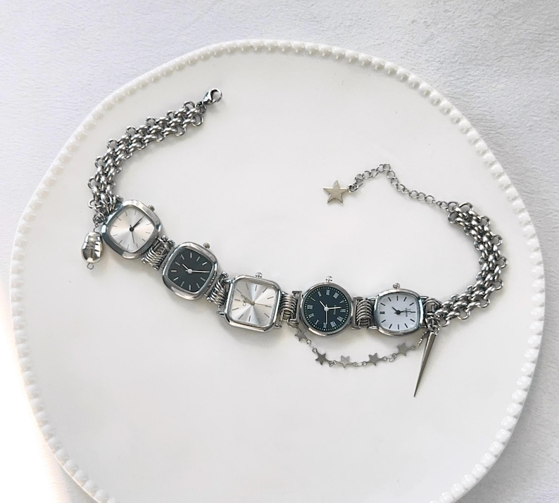 May include: A silver chain bracelet with four square watch faces. The watch faces have black hands and black numbers. The bracelet has a star charm and a small silver spike charm.
