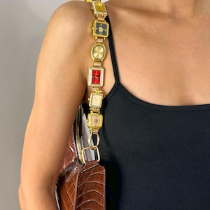 May include: A brown, textured handbag with a gold chain strap made of square-faced watches. The watches have various colored faces, including yellow, black, and red. The bag is carried over the shoulder.