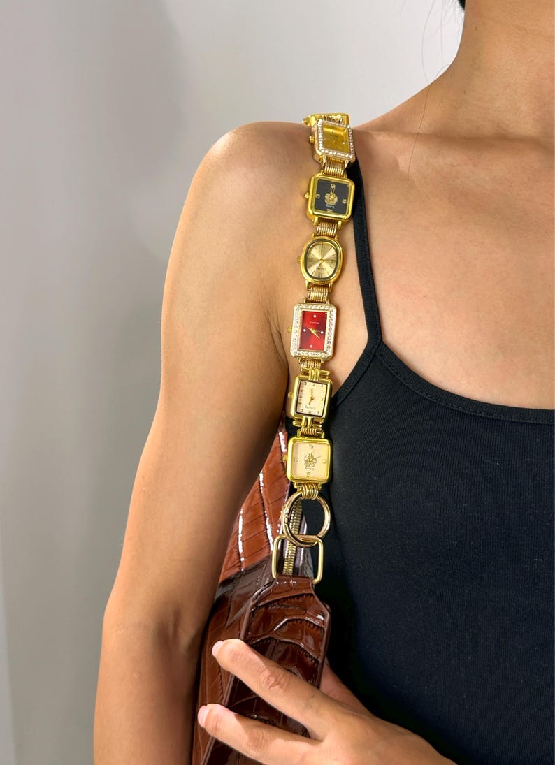 May include: A brown handbag with a gold watch strap. The strap is made of multiple gold-toned square and rectangular watch faces, some with gemstones. The bag has a crocodile skin texture.