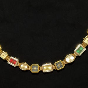 May include: A gold-toned bracelet featuring a series of rectangular and oval watch faces. The watch faces display various colors, including red, green, and black, and are adorned with gemstones. The bracelet has two circular clasps.