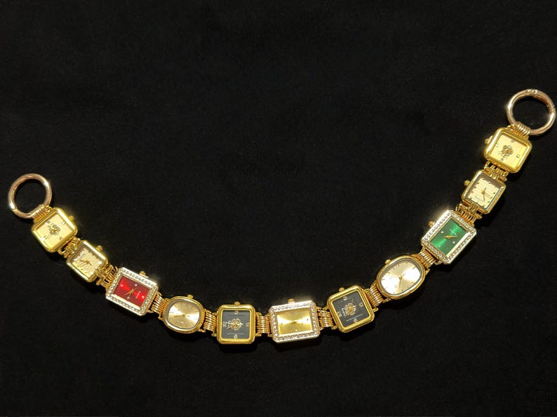 May include: A gold-toned bracelet featuring a series of rectangular and oval watch faces. The watch faces display various colors, including red, green, and black, and are adorned with gemstones. The bracelet has two circular clasps.