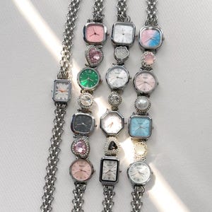 May include: Three silver chain link bracelets with different colored square watch faces and charms. The charms include a heart, a pearl, a crystal, and a flower.