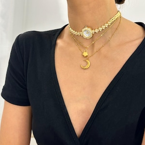 Può includere: Un set di collane a strati in oro con un ciondolo a forma di orologio, un ciondolo a forma di stella e un ciondolo a forma di mezzaluna.