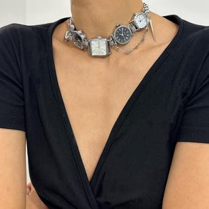 May include: A silver choker necklace with multiple small watch faces attached. The necklace is made of metal and has a delicate chain design.