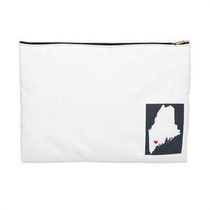 May include: White zippered pouch with a black zipper and gold-colored pull. A navy blue square with a white outline of the state of Maine and a red heart is in the lower right corner. The pouch is rectangular.