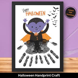 May include: A framed Halloween-themed artwork featuring a cartoon vampire with a handprint body. The vampire has a purple face, black hair, and an orange cape. The words "Happy Halloween" are above the vampire, with bats flying above.