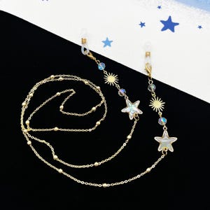 Könnte beinhalten: Eine goldene Kette mit Stern- und Sonnenanhängern, perfekt zum Halten von Brillen oder einer Maske.