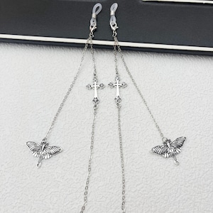 May include: Silver-toned eyeglass chain featuring two clear rubber loops for attachment. The chain has decorative crosses and butterfly charms. The chain is designed to hang around the neck and keep glasses secure.