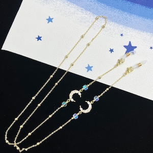 Puede incluir: Portagafas de cadena dorada con cuentas de cristal iridiscente y dijes de luna creciente.