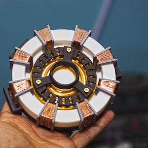 May include: A white and gray circular device with copper-colored coils. The device has a black center with a gold ring around it.