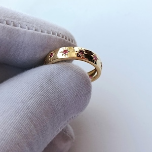 May include: A gold band ring with a row of small red gemstones set in star-shaped settings.