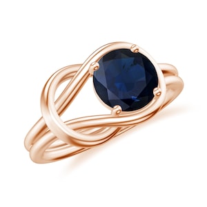 May include: A rose gold ring with a knotted band and a round, dark blue gemstone.