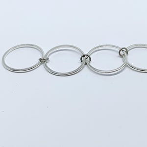 Puede incluir: Una pulsera plateada con cuatro eslabones circulares interconectados. Los eslabones est&aacute;n unidos por peque&ntilde;os cierres circulares. La pulsera se muestra sobre una superficie blanca, resaltando su dise&ntilde;o simple y moderno. Adecuada para uso diario.