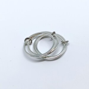 Puede incluir: Un colgante de anillos entrelazados de color plateado. El colgante consta de tres anillos circulares conectados. Los anillos son lisos y brillantes, con un dise&ntilde;o sencillo y elegante. El colgante se muestra sobre un fondo blanco.