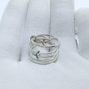 Puede incluir: Un anillo plateado con m&uacute;ltiples bandas conectadas por peque&ntilde;os aros. El anillo, hecho de metal brillante, descansa sobre una superficie blanca. El dise&ntilde;o es minimalista y moderno, adecuado para el uso diario.