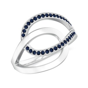 May include: A silver ring with a unique, intertwined design. The ring features a series of small, round, dark blue gemstones set along the edges of the intertwined loops. The ring has a polished, reflective surface.