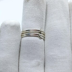 Puede incluir: Un anillo plateado con un dise&ntilde;o minimalista. El anillo presenta cuatro bandas finas unidas por peque&ntilde;os conectores verticales. Las bandas son lisas y brillantes, reflejando la luz. El anillo se muestra sobre un fondo blanco.