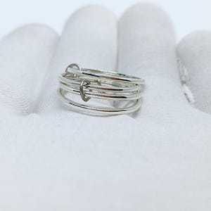 Puede incluir: Un anillo de plata con un dise&ntilde;o &uacute;nico. El anillo presenta m&uacute;ltiples bandas finas conectadas por peque&ntilde;os eslabones curvos. Las bandas son lisas y brillantes, reflejando la luz. El anillo est&aacute; sobre un fondo blanco.