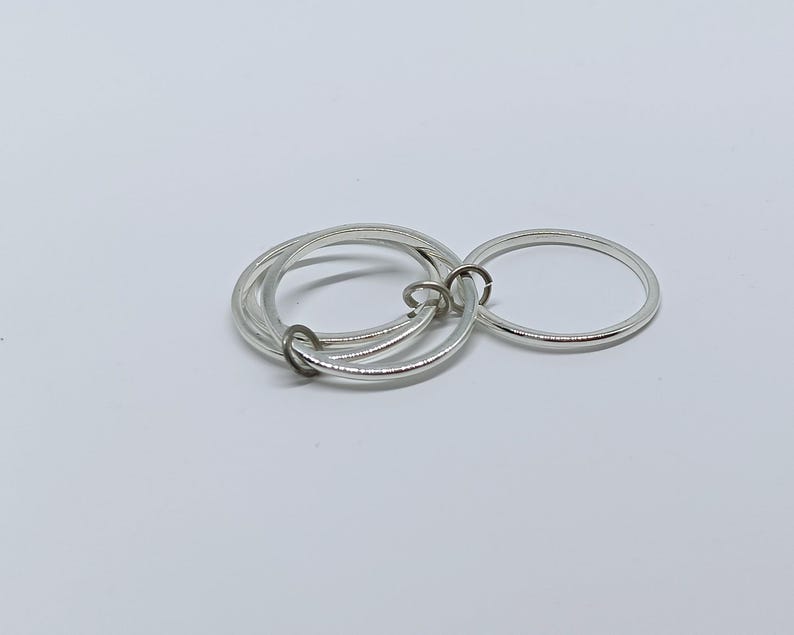 Puede incluir: Un conjunto de anillos plateados, que incluye tres anillos entrelazados y un anillo separado. Los anillos est&aacute;n hechos de un material met&aacute;lico brillante y est&aacute;n dispuestos sobre una superficie blanca. Probablemente sean joyas.