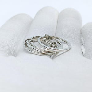 Puede incluir: Un anillo plateado con m&uacute;ltiples bandas entrelazadas. El anillo est&aacute; hecho de un metal brillante y reflectante y se muestra sobre una superficie blanca. El dise&ntilde;o presenta varios c&iacute;rculos conectados, creando un aspecto &uacute;nico y moderno.