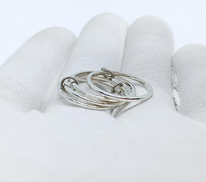 Puede incluir: Un anillo plateado con m&uacute;ltiples bandas entrelazadas. El anillo est&aacute; hecho de un metal brillante y reflectante y se muestra sobre una superficie blanca. El dise&ntilde;o presenta varios c&iacute;rculos conectados, creando un aspecto &uacute;nico y moderno.