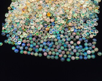 Op de afbeelding: Een grote stapel iriserende opaal cabochons in verschillende tinten blauw, groen en wit. De cabochons zijn rond en hebben een gladde, gepolijste afwerking.
