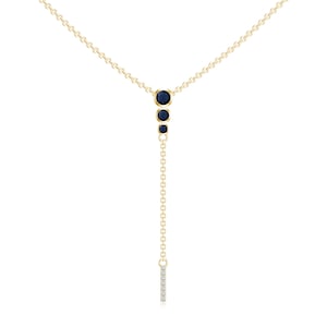 Op de afbeelding: Een gouden ketting met een hangende ketting en een kleine staaf met diamanten aan het einde. De ketting heeft drie blauwe edelstenen in een aflopende maat.