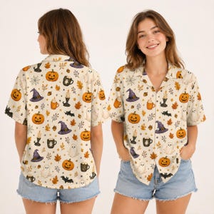 Puede incluir: Una camisa de manga corta con botones y un estampado integral de calabazas naranjas, sombreros de bruja morados, fantasmas blancos, murciélagos negros, hojas de otoño marrones, velas y tazas sobre un fondo crema, vista frontal y trasera.