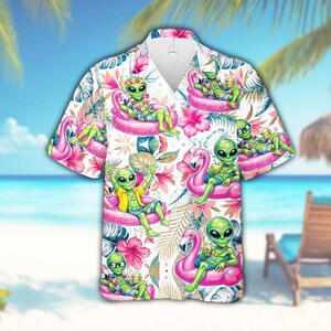 May include: Short-sleeved button-down shirt featuring a tropical pattern with green aliens relaxing on pink flamingo floats. The shirt has a white background with pink flowers and green leaves, perfect for a summer vacation.