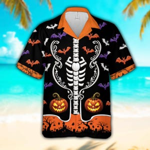 Puede incluir: Una camisa de manga corta con botones sobre fondo negro, con un estampado de caja torácica esquelética blanca, calabazas naranjas y murciélagos morados y blancos. Cuello y dobladillo naranja con una silueta negra de un cementerio.