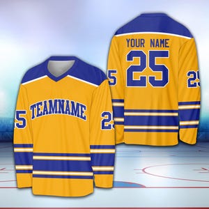 May include: A gold hockey jersey with blue and white stripes. The jersey has the number "25" and the text "YOUR NAME" on the back. The front of the jersey has the text "TEAMNAME" and the number "25" on the sleeves.