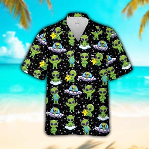 May include: Black short-sleeved button-down shirt with a repeating pattern of green aliens, UFOs, stars, and clouds. The aliens are depicted in various poses, some holding stars or globes. The shirt has a classic collar and a relaxed fit.