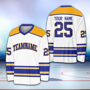 May include: White hockey jersey with blue and gold stripes. The jersey has a gold collar and a gold nameplate with the text "YOUR NAME" and the number "25" in blue. The jersey also has a blue nameplate with the text "TEAMNAME" in gold.