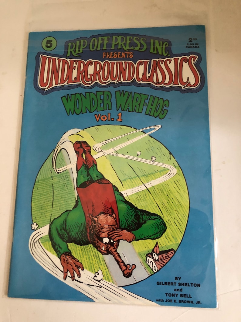 May include: A comic book cover featuring a green and red cartoon character flying through the air. The cover is blue with white text that reads "Rip Off Press Inc. Presents Underground Classics Wonder Wart Hog Vol. 1". The text at the bottom of the cover reads "By Gilbert Shelton and Tony Bell with Joe E. Brown, Jr."
