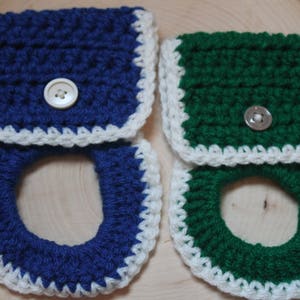 May include: Two crocheted toilet paper roll holders, one blue and white and one green and white. Both have a white crocheted trim and a white button.