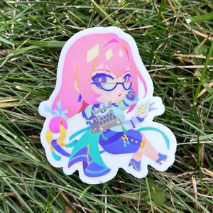 May include: A sticker featuring a cartoon character with pink hair, blue eyes, and glasses. The character is wearing a blue and green outfit and holding a blue and white staff. The sticker is on a green grassy background.