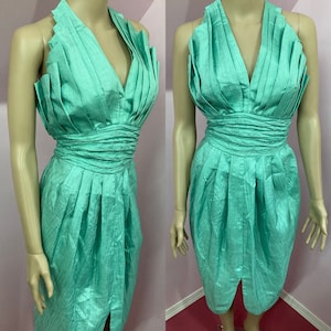 May include: A mint green halter dress with a pleated bodice and a fitted skirt. The dress has a deep V-neckline and a slit in the front.
