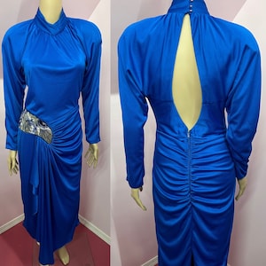 May include: A royal blue long-sleeved dress with a high neckline and a keyhole back. The dress has a ruched design and a silver sequined embellishment on the side.