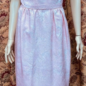 May include: A pink sleeveless dress with a floral pattern. The dress has a fitted bodice and a flowing skirt with a slit in the front.